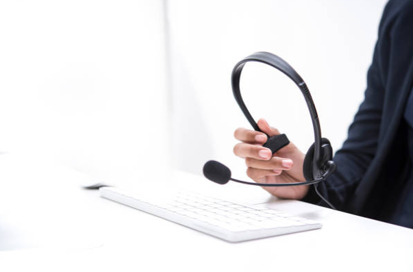 Mão de atendente de call center apoiada sobre a mesa com um teclado. A mão segura um headset.