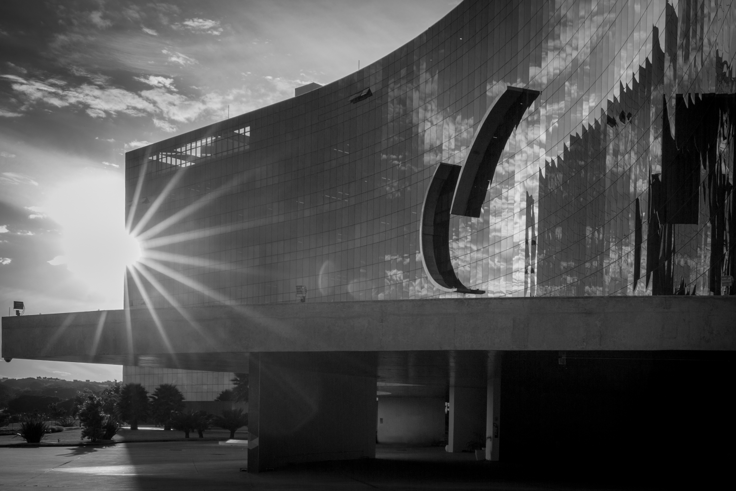 Foto em preto e branco da fachada do edifício-sede com raios do sol ao fundo.