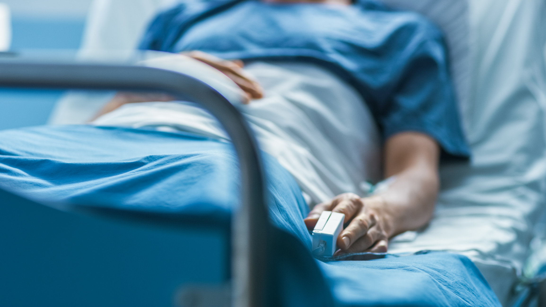 Pessoa deixada em uma cama de hospital com um pregador de oxímetro no dedo.