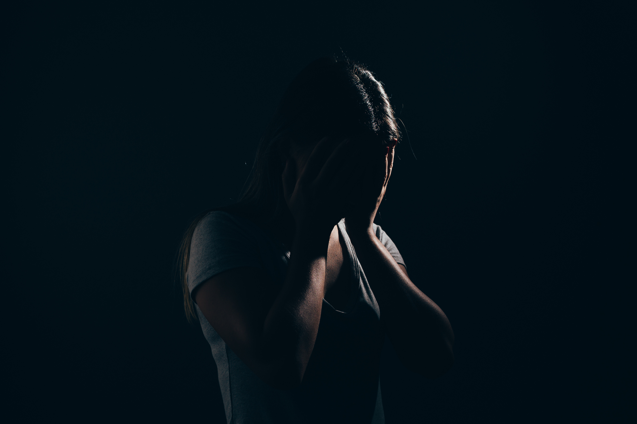 Imagem: mulher em meio a ambiente escuro, cobrindo o rosto com as mãos