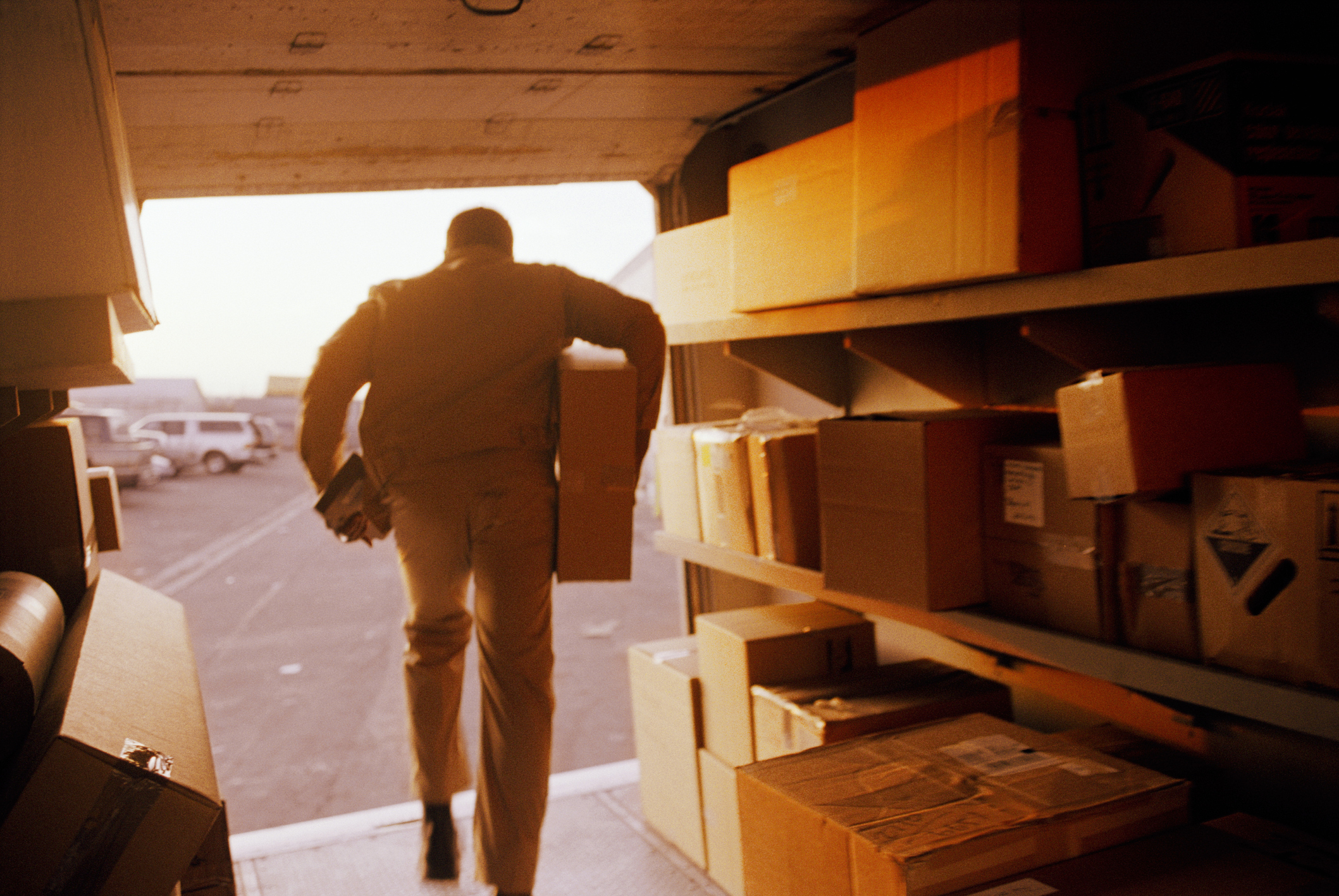 Imagem: homem carregando caixas enquanto sai de carro