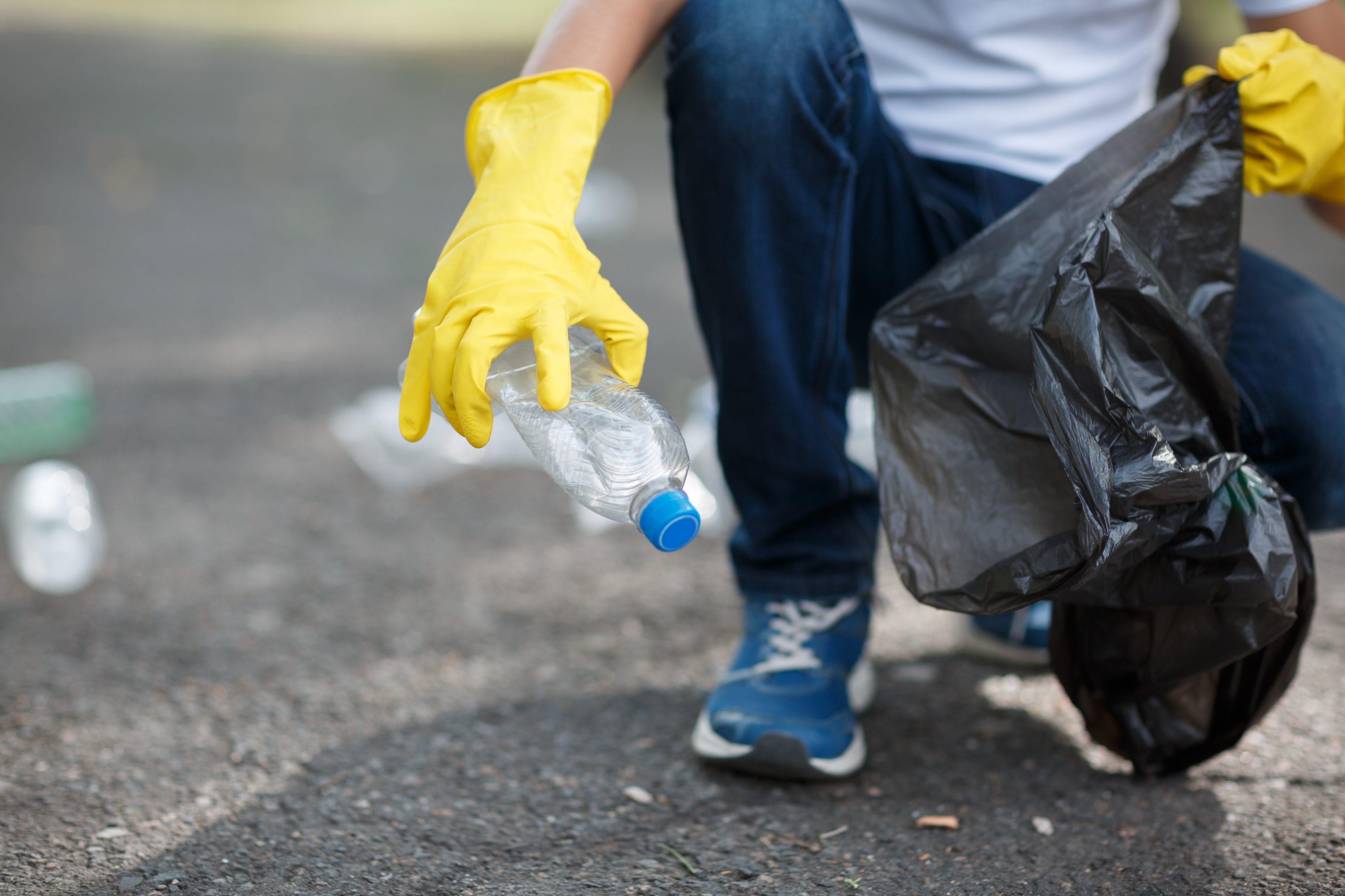 Pessoa com um saco de lixo coletando uma garrafa plástica do chão.