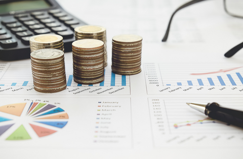 Imagem: moedas e calculadora sob papéis com gráficos