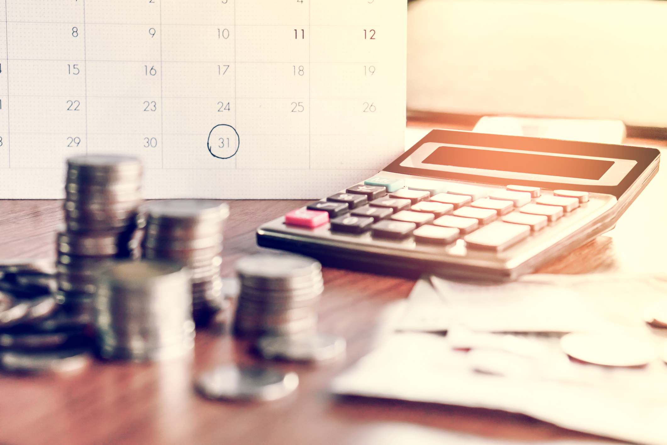 Sobre a mesa: um calendário, moedas, uma calculadora e papeis. 