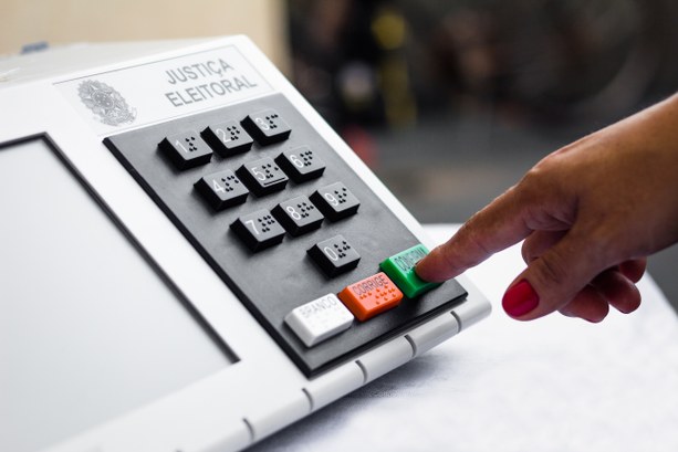 Mão feminina apertado a tecla confirma da urna eletrônica brasileira. (Foto: Justiça Eleitoral)