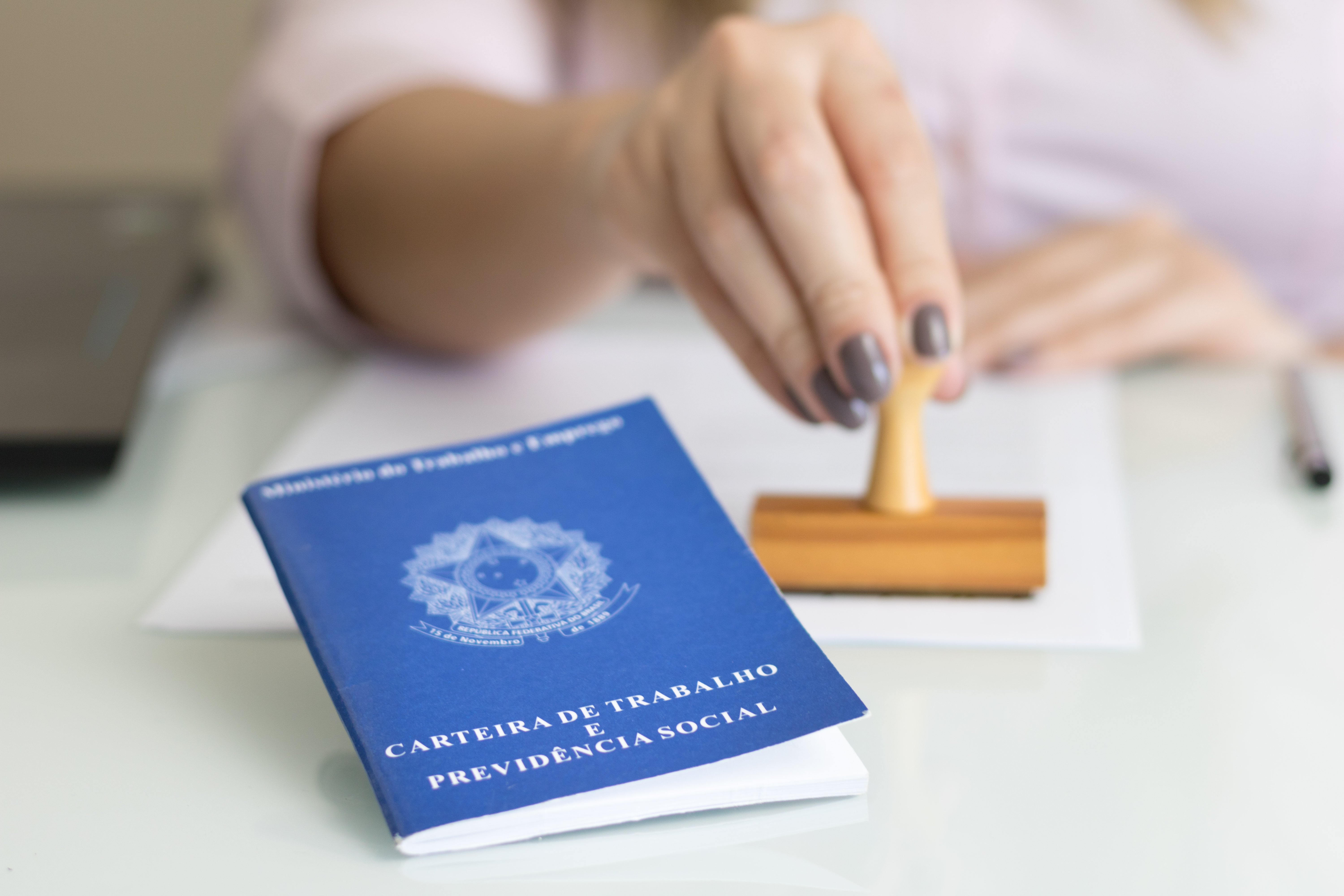 CTPS sobre a mesa com uma mão segurando um carimbo ao fundo.