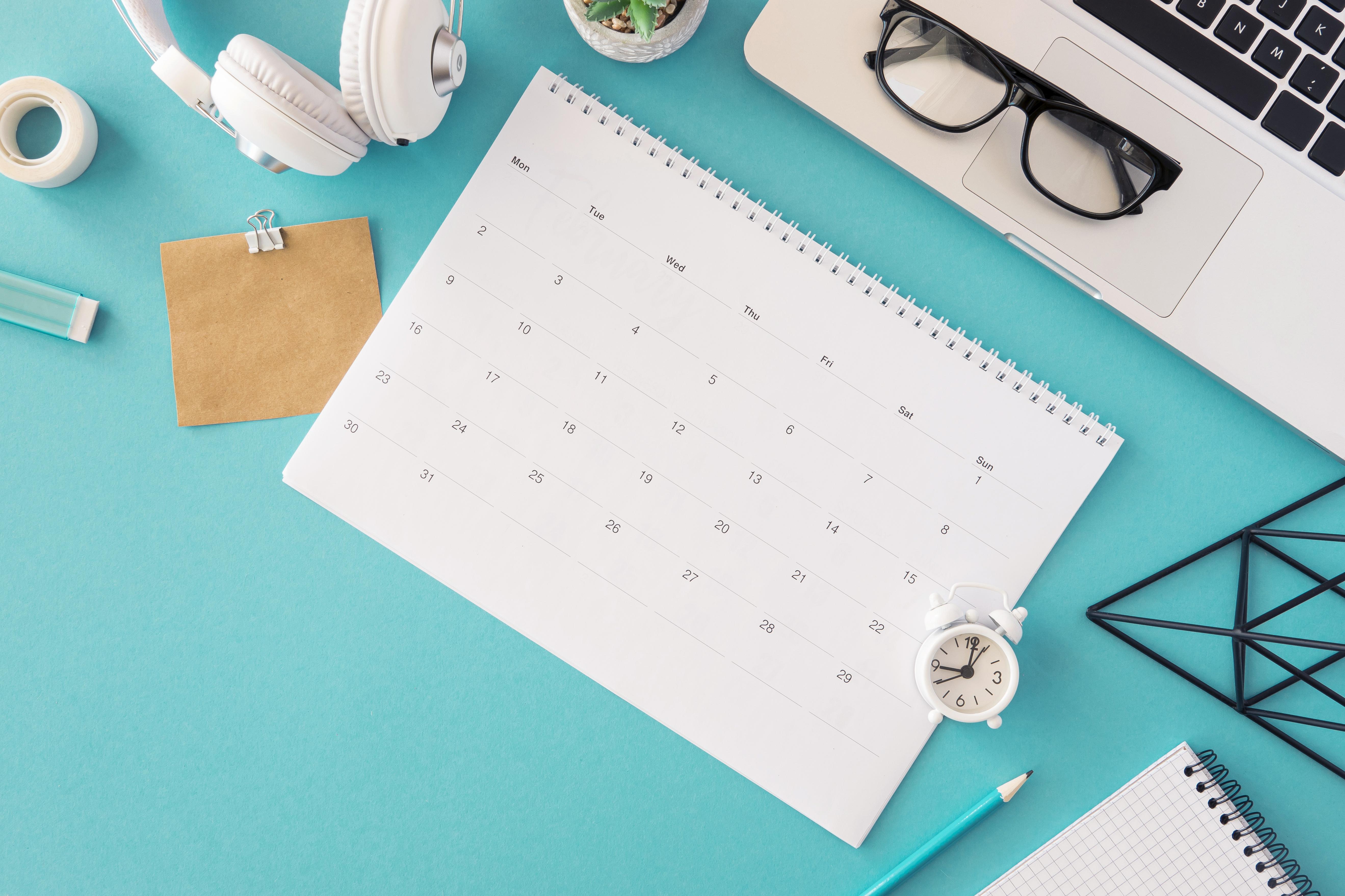 Mesa com calendário, notebook, fones de ouvido, entre outros objetos.