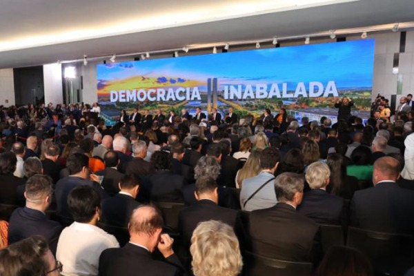 Foto de pessoas em evento no Congresso Nacional. No painel está escrito: Democracia Inabalada.