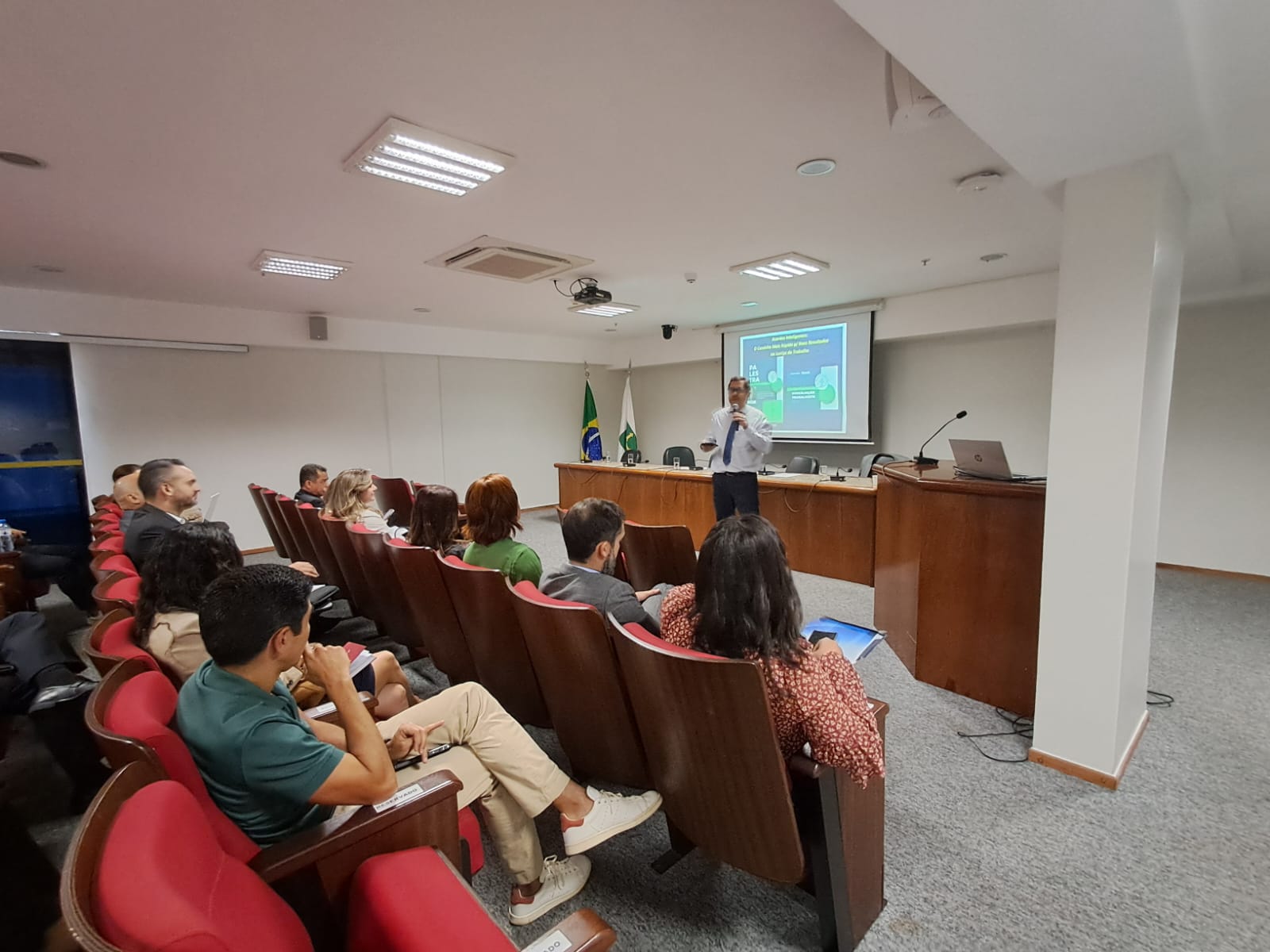 Fotografia da palestra com a presença de pessoas sentadas e o palestrante fazendo o discurso. 