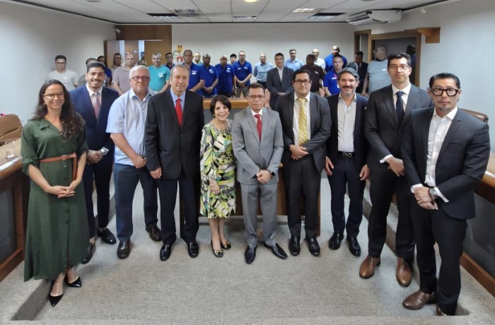 Grupo de pessoas vestidas com traje social a frente e outro grupo de pessoas atrás vestidas com um uniforme azul.