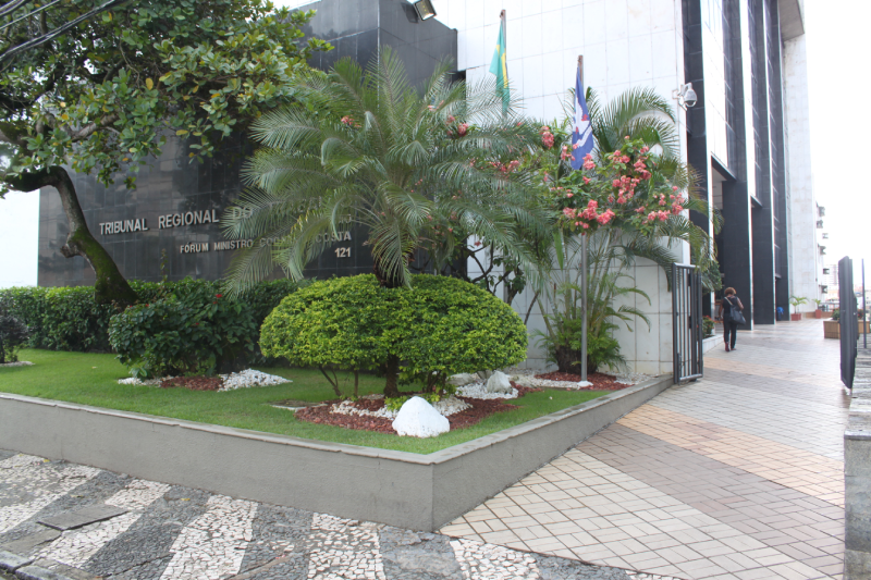 Foto da fachada do TRT-5. com plantas e um coqueiro/palmeira no jardim