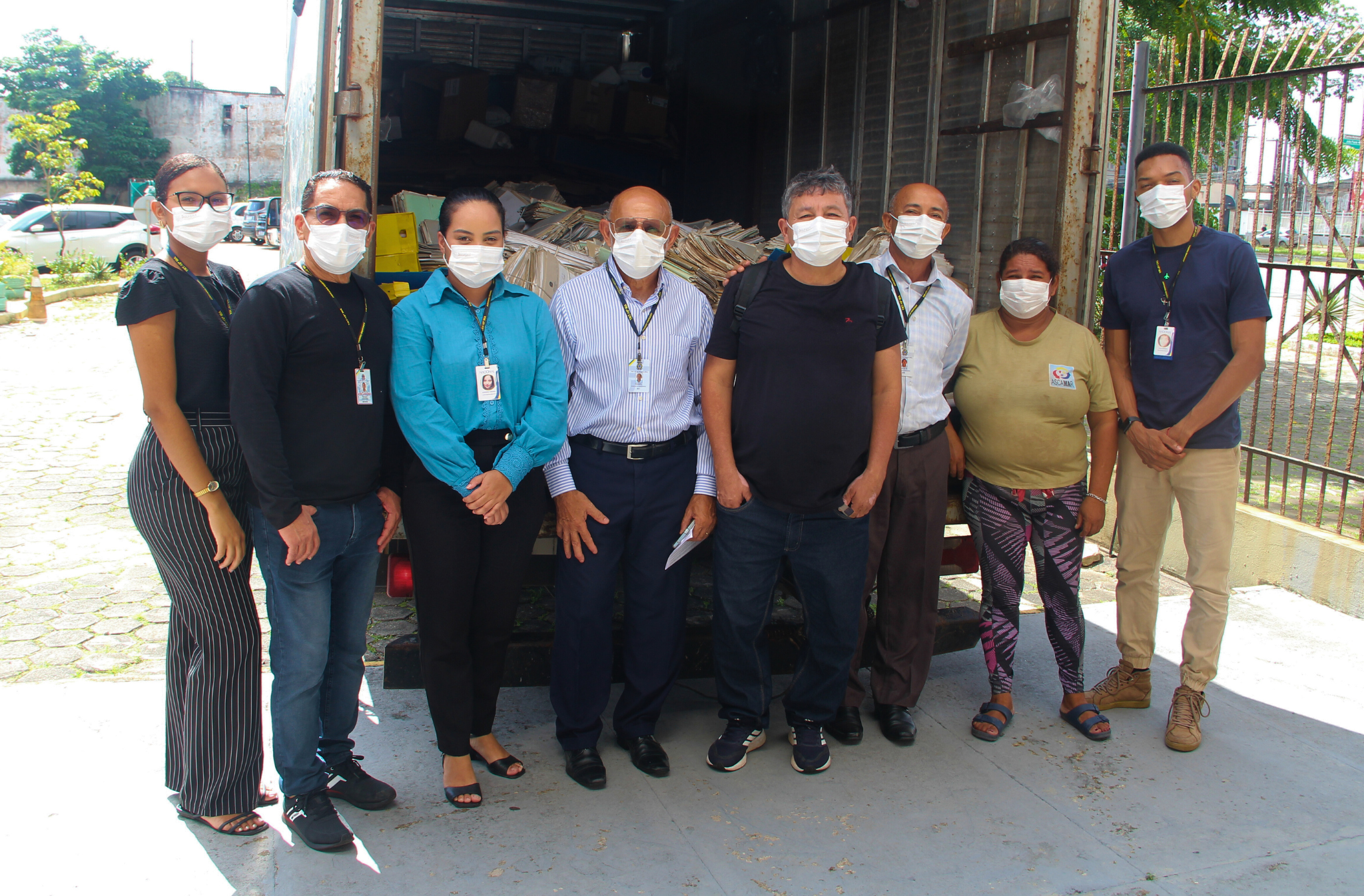 Foto de servidores posicionados diante de um caminhão carregado de processos antigos descartados para reciclagem.