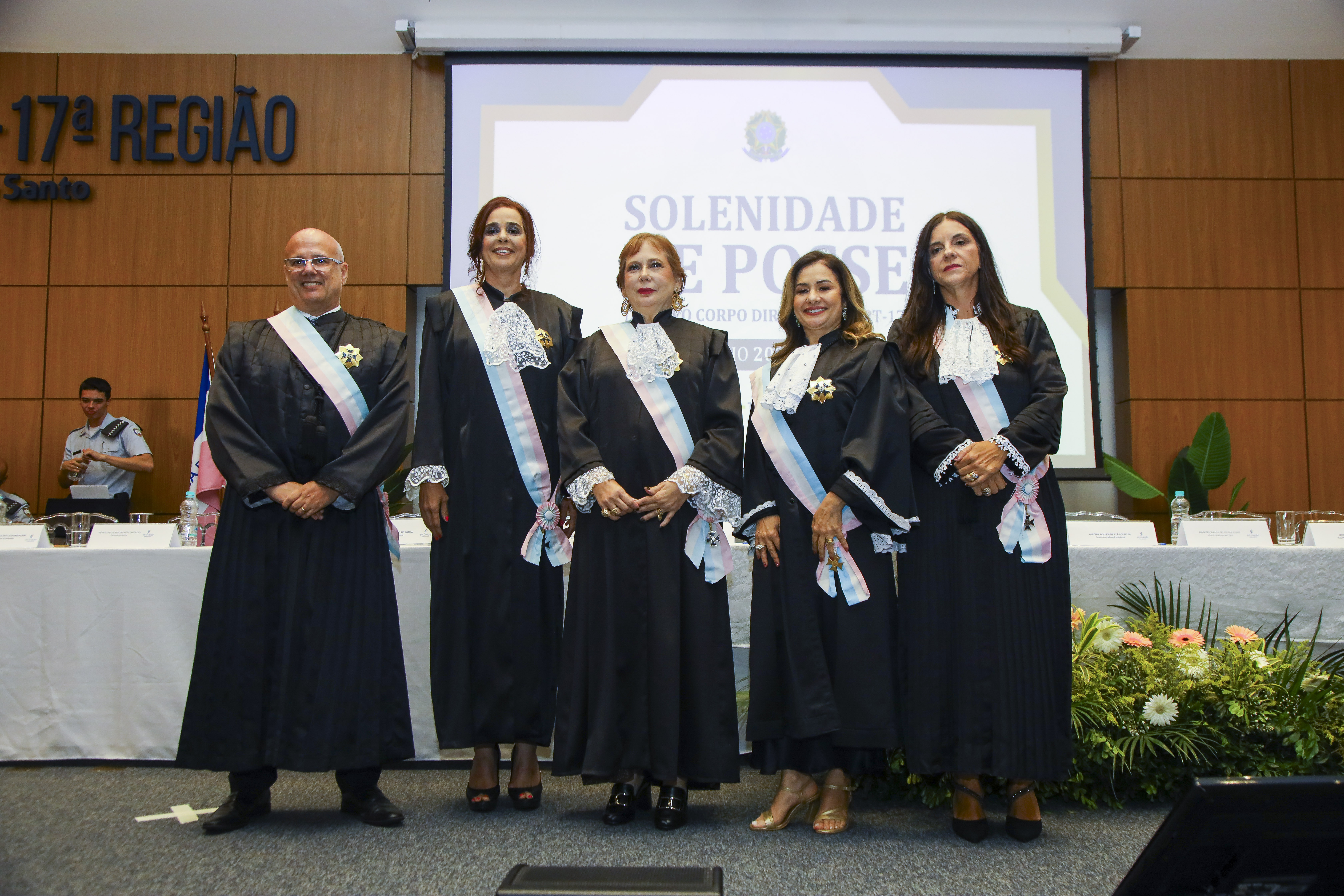 Fotografia com 4 mulheres e 1 homem usando uma faixa com as cores rosa, branco e azul.