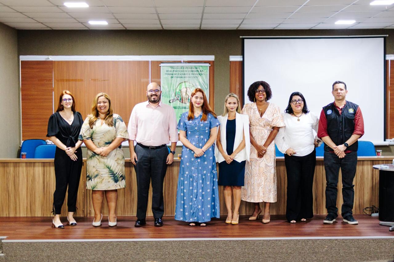 Fotografia com 6 mulheres e 2 homens em frente ao banner.