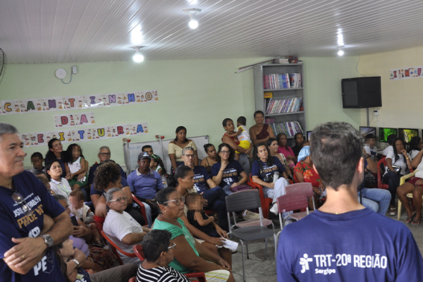 Fotografia com a presença de um público sentado e uma pessoa com a camisa do TRT-20ª Região Sergipe.