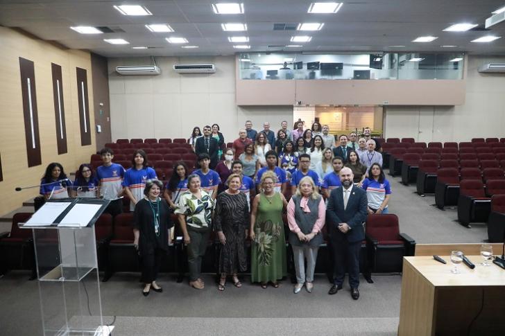 Fotografia colorida em ambiente fechado reunindo homens e mulheres, todos estão em pé sorrindo para a foto. — Foto: ASCOM8