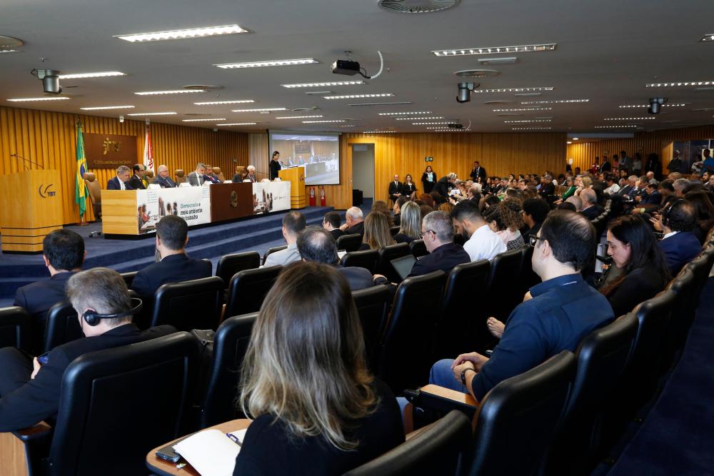 Foto em diagonal do auditório registrando o publico sentado nas cadeiras e a mesa de abertura com diversas autoridades. 