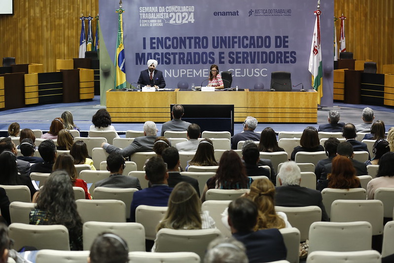 Auditório com cadeiras lotadas e o palestrante indiano sentado na mesa.
