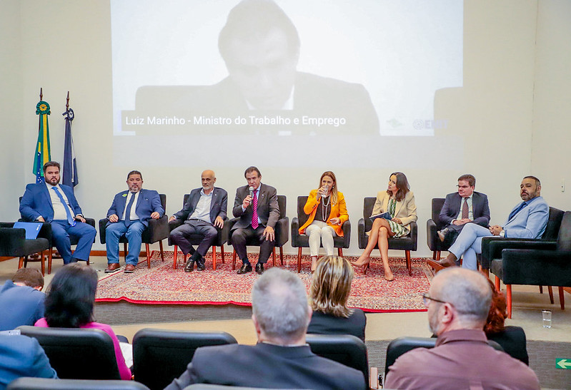 Auditório com pessoas sentadas em cadeiras no palco.