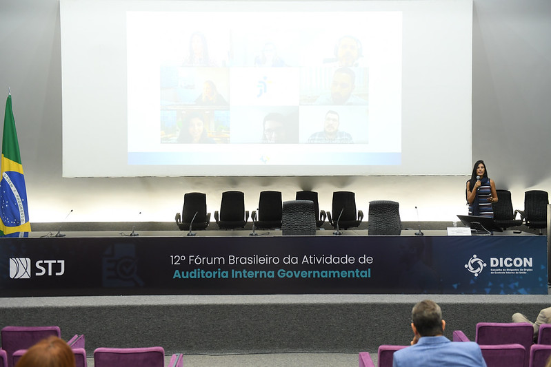 Foto do palco do auditório com a servidora fazendo a apresentação.