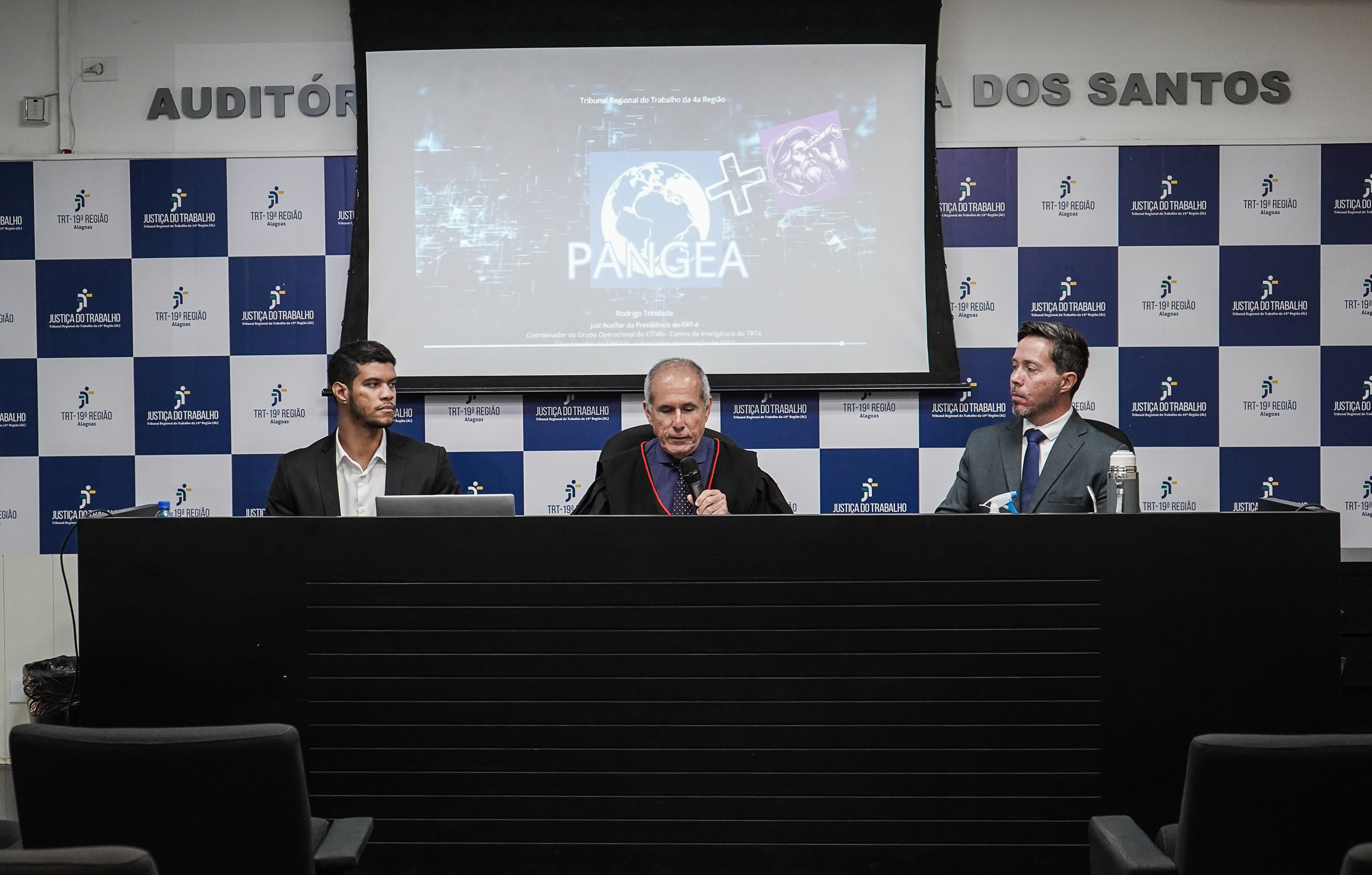 Fotografia com três homens no palanque falando sobre a adoção do sistema Pangea no TRT-19 (AL) 