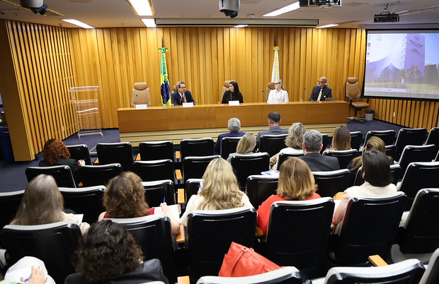 Foto do auditório com os participantes olhando pra mesa de abertura.