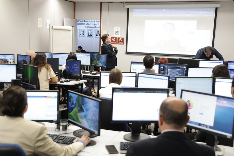 Foto do laboratório onde os participantes estavam reunidos. Diversas pessoas e computadores.