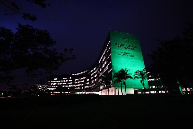 Foto do edificio-sede do TST e do CSJT iluminado de verde durante a noite.