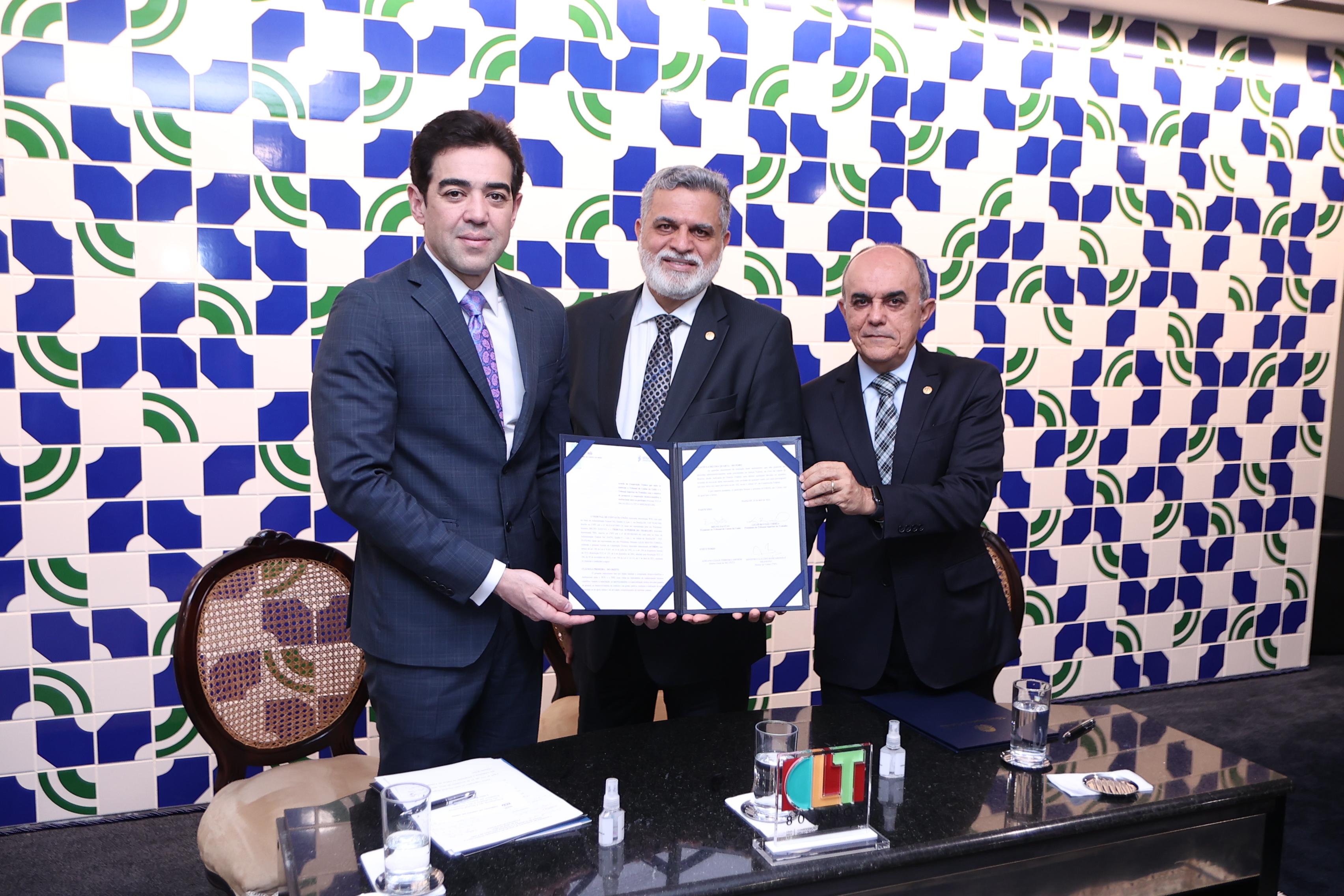 Ministros Bruno Dantas, Lelio Bentes e Cláudio Brandão segurando o acordo assinado