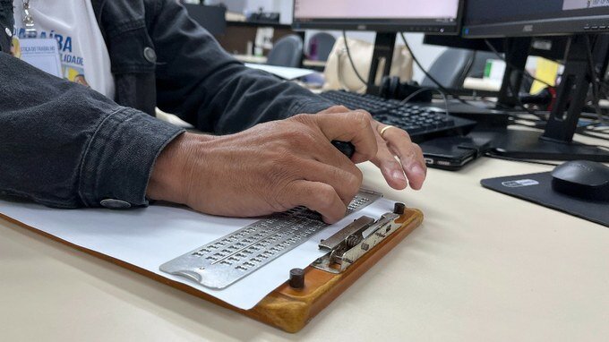 Fotografia de um funcionário do TRT-13 teclando um manual em braile.