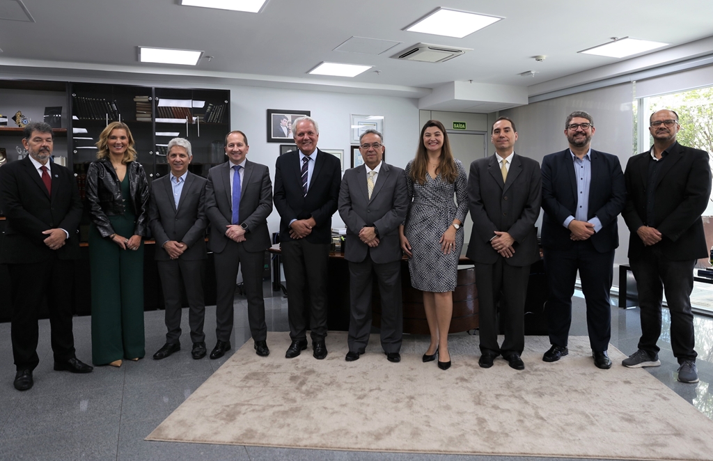 Uma fotografia de um grupo de dez pessoas, incluindo oito homens e duas mulheres, todos adultos, de pé lado a lado em um ambiente de escritório.