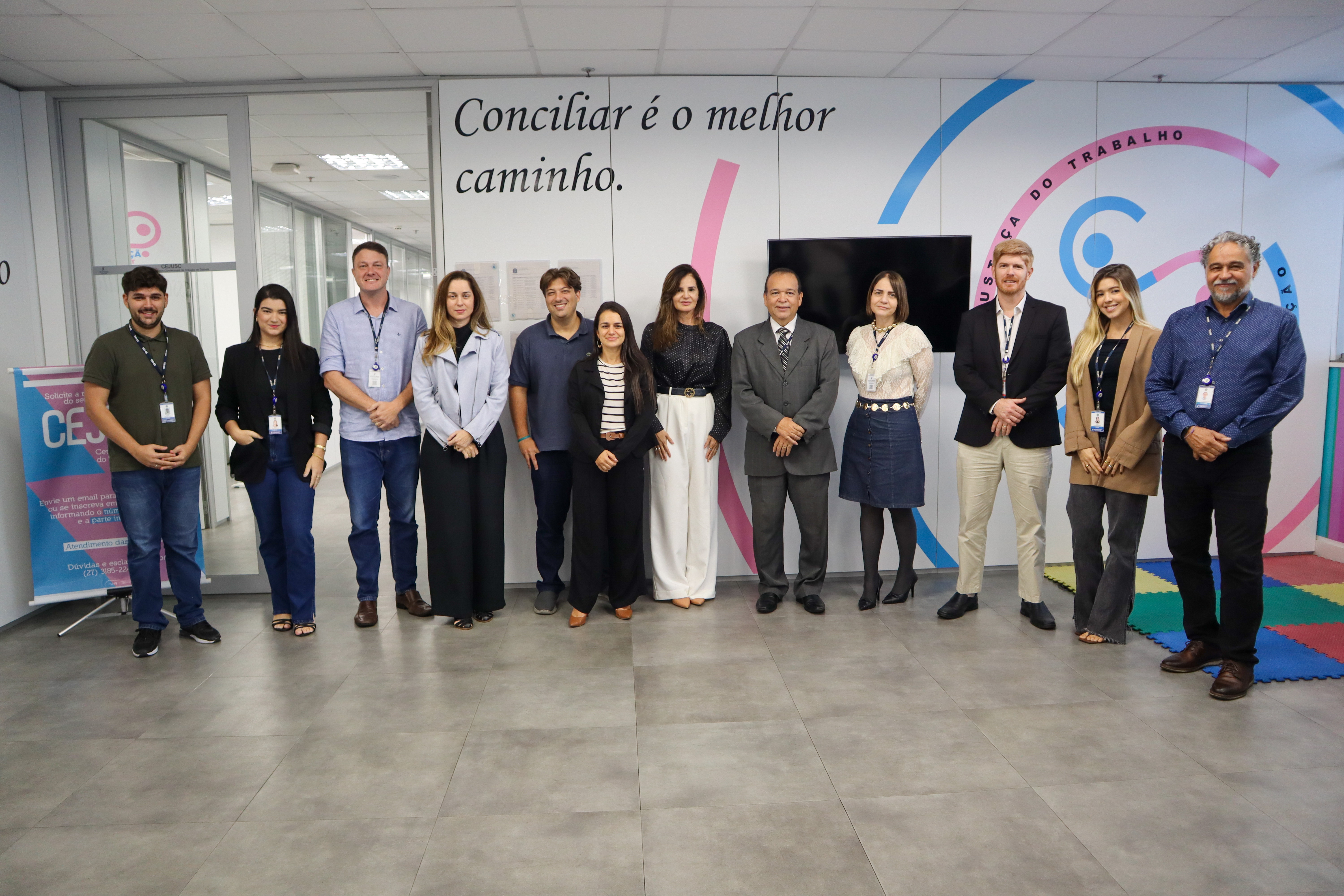 A imagem mostra um grupo de pessoas posando para foto em frente a uma parede com a frase