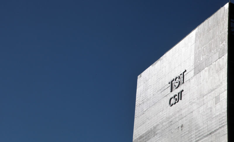 Foto da quina da fachada de concreto do TST e do CSJT em perspectiva para ter o céu azul como destaque. A quina compõe comente um lado da foto.