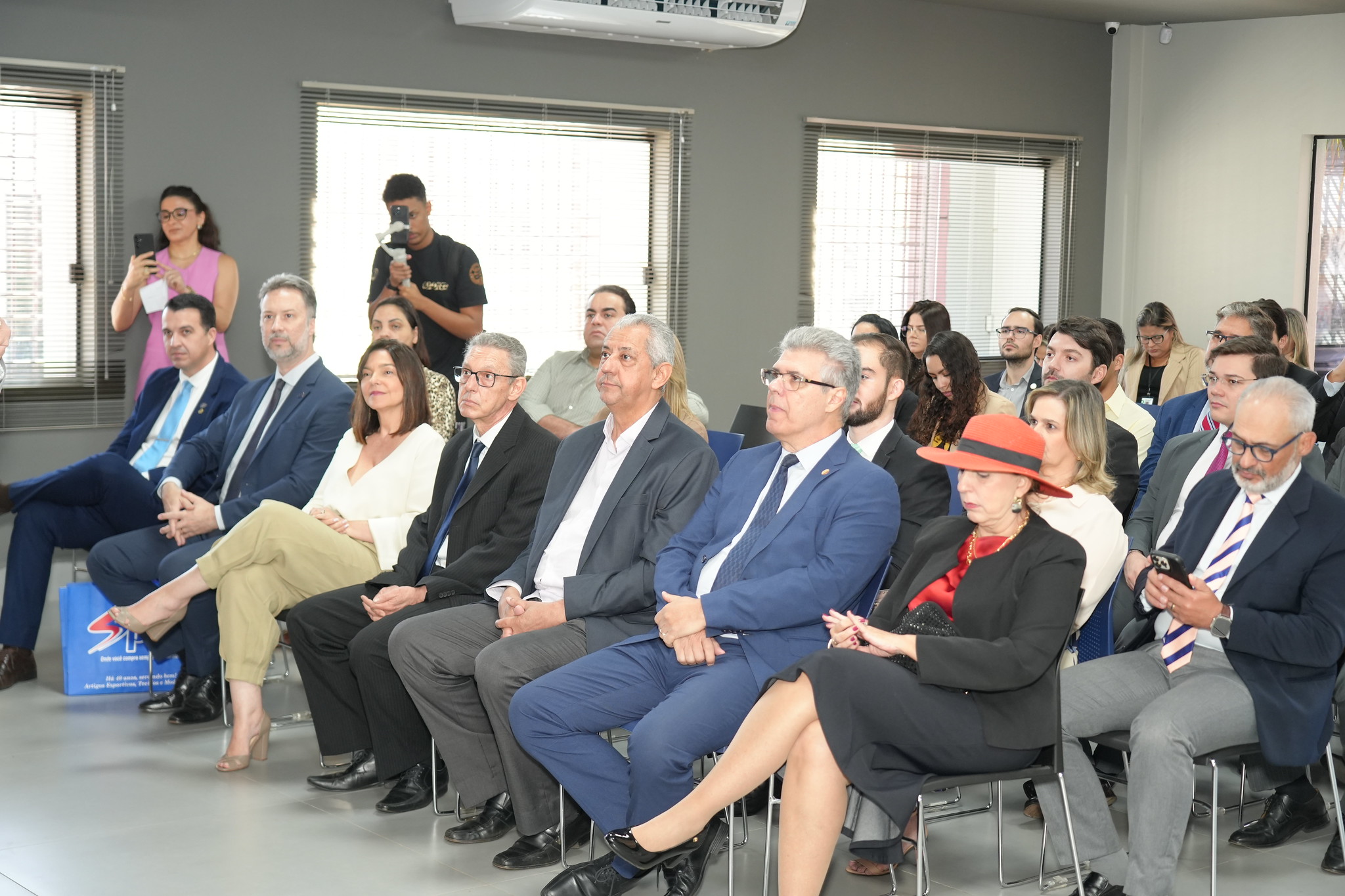 Várias pessoas sentadas em um auditório. Elas usam roupas formais.