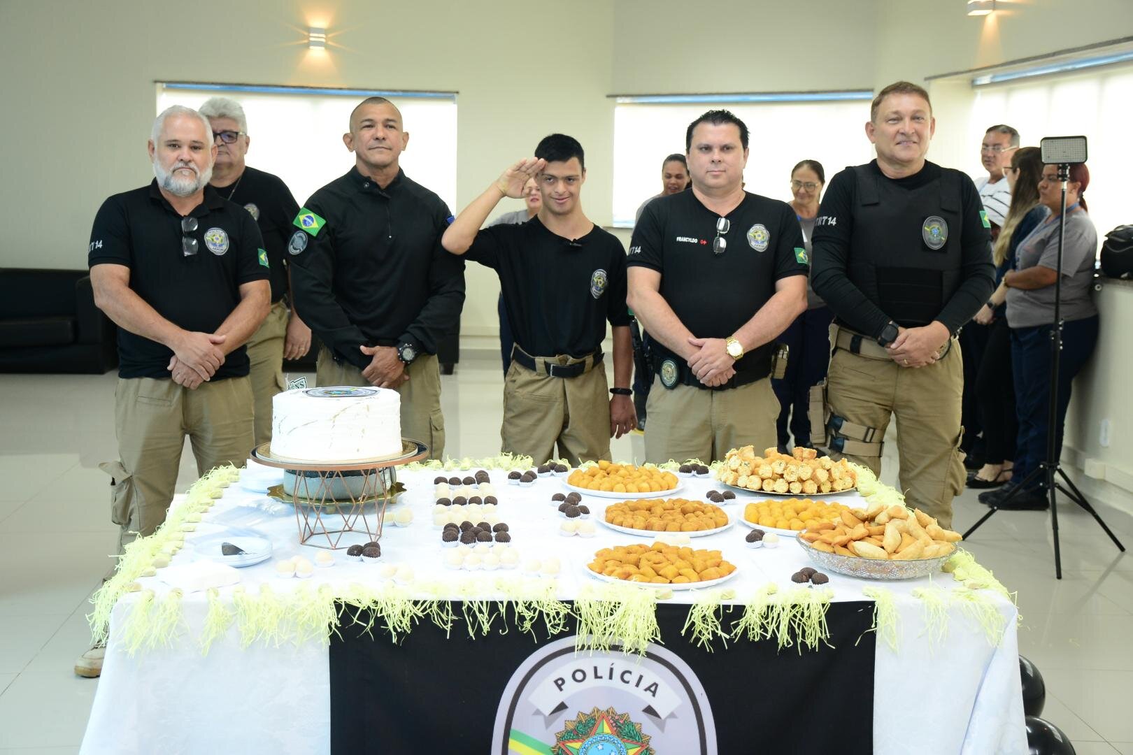 Fotografia com 5 homens com a roupa de policial em destaque e um deles, no meio, é um jovem com síndrome de Down que realizou sonho de ser policial por um dia.