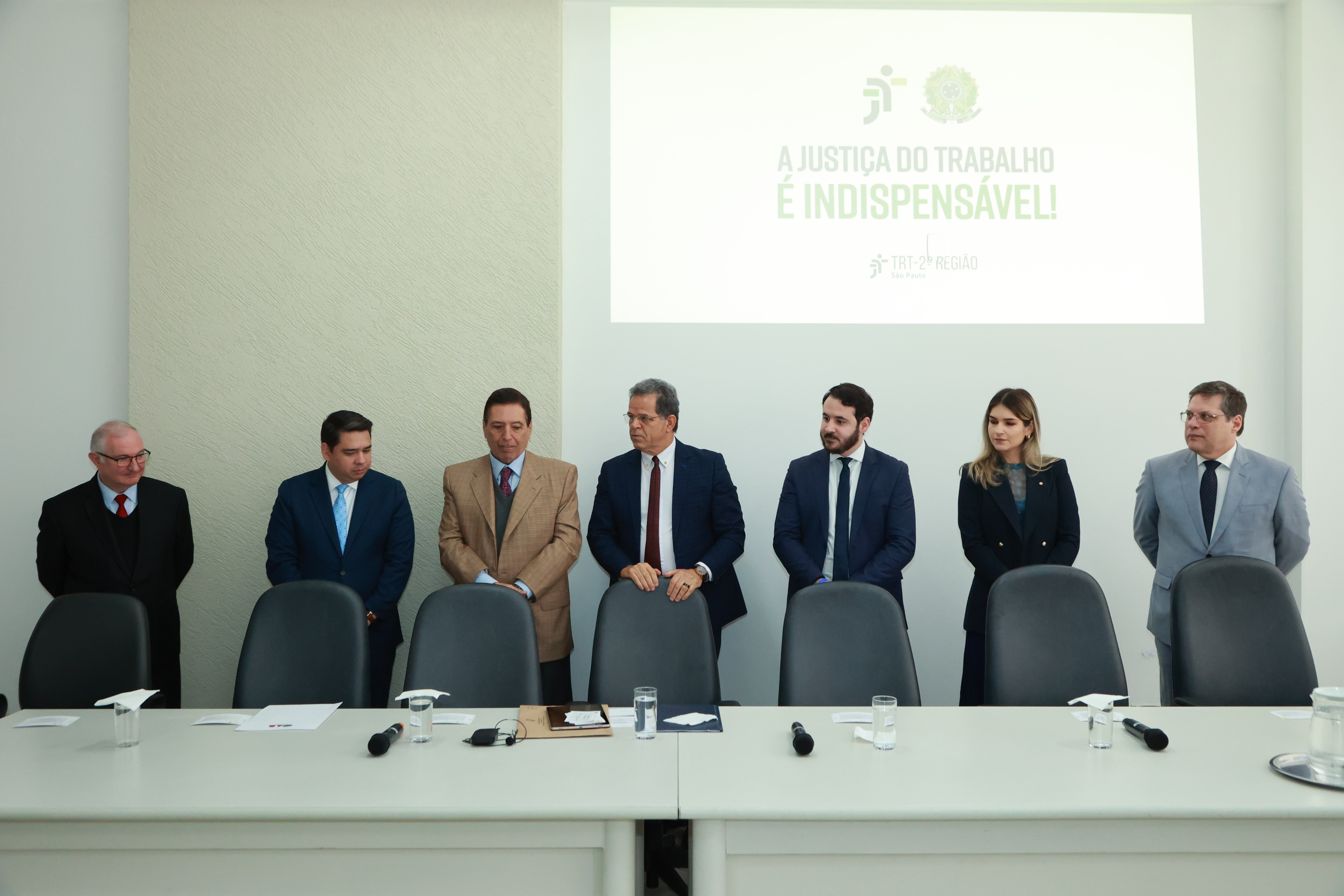 Autoridades em pé durante evento institucional do TRT da 2ª Região, com a frase “A Justiça do Trabalho é indispensável!” projetada ao fundo.