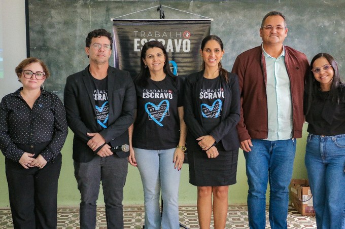 Seis pessoas posam para foto em frente a um banner com o tema