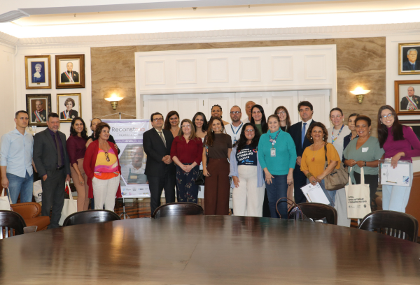 Grupo de pessoas em pé ao fundo de uma sala. 