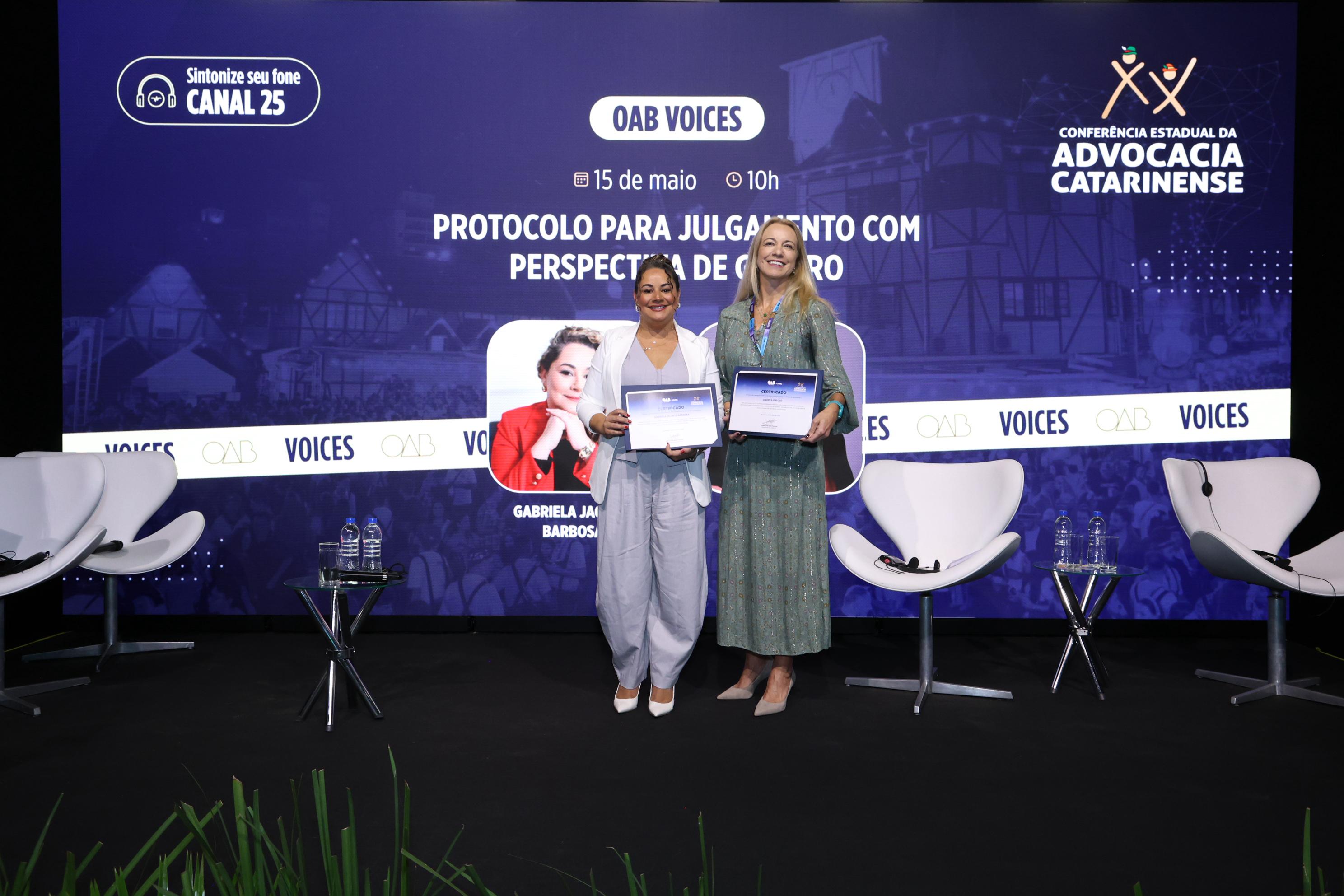 Duas mulheres posam com certificado nas mãos.