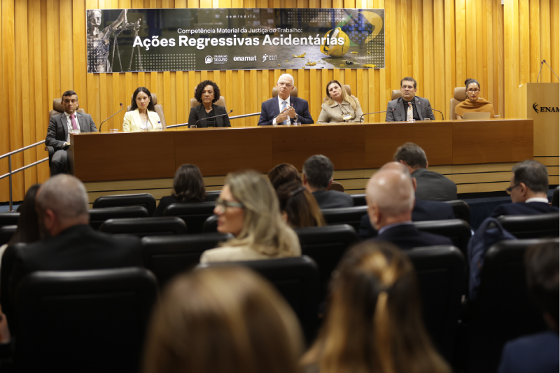 Foto dos gestores nacionais na mesa do auditório ouvindo a fala de um dos gestores regionais na plateia.