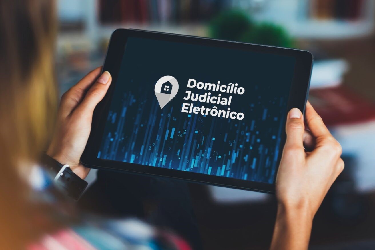 Mulher segurando um tablet. Na tela, a logo do Domicilio Judicial Eletrônico.
