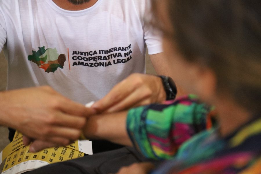 Pessoa com a camisa da itinerância colando uma pulseira em uma pessoa atendida durante ação do CNJ na região amazônica.