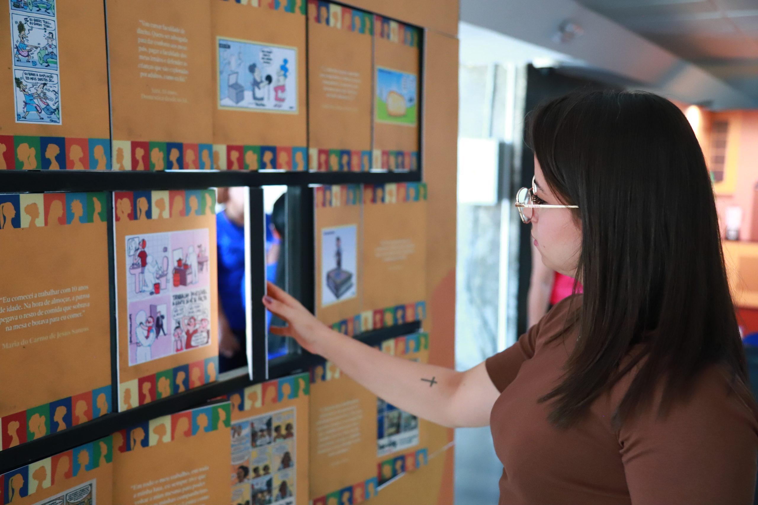 Foto de uma mulher olhando os mini painéis rotativos da exposição no TRT de Goiás.