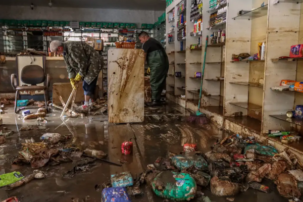 Dois homens limpando uma farmácia suja de lama.
