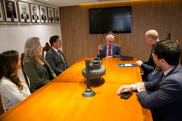 Fotografia de uma mesa com 7 pessoas sentadas, 4 homens e 3 mulheres. 