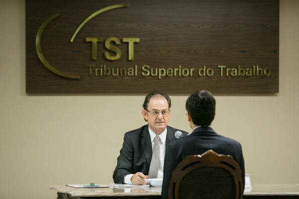 Ministro do TST Hugo Carlos Scheuermann sentado e recebendo candidato que fará sorteio dos pontos para a prova oral.