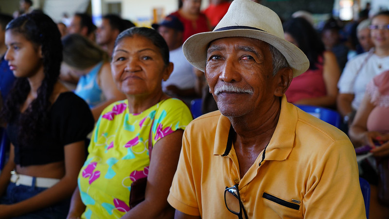 Casal com homem pardo, cabelos e bigode grisalhos e chapéu branco, ao lado de mulher parda com cabelo preso e vestido estampado. Ambos estão entre as pessoas atendidas na itinerância promovida em Araguatins.