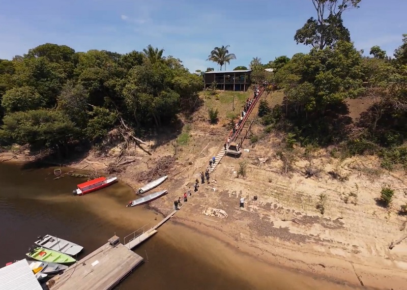 Foto aerea da comitiva subindo as escadas na beira do rio para acessar a comunidade.