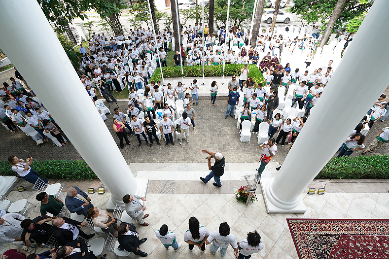 Foto tirada de cima dos alunos nos jardins da sede do TRT-7 (CE) prestando atenção na fala do rapper.