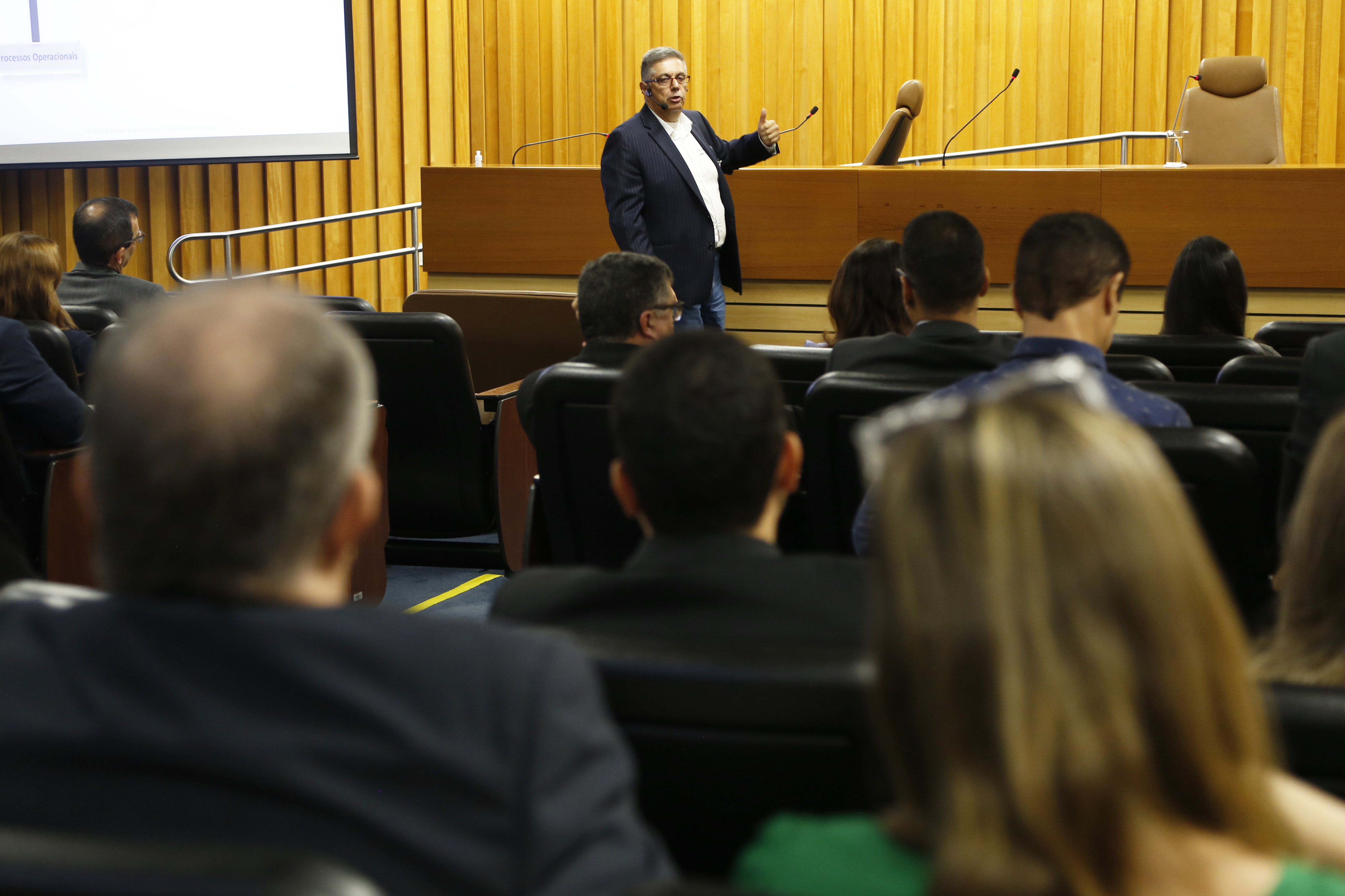 Professor de auditoria interna Eduardo Person Pardini gesticulando, enquanto as pessoas na plateia observam. Ele está de terno, camisa branca e sem gravata. É um home de cabelos grisalhos e usa óculos.
